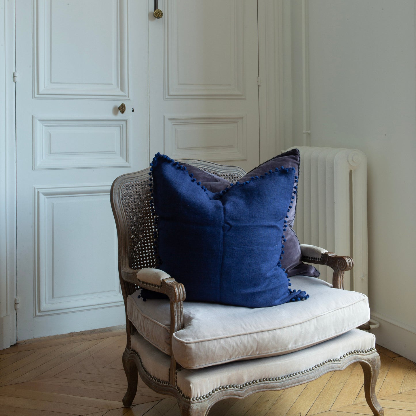 Housse de coussin en lin brut bleu marine 60 × 60 cm bordée de pompons sur un fauteuil ancien